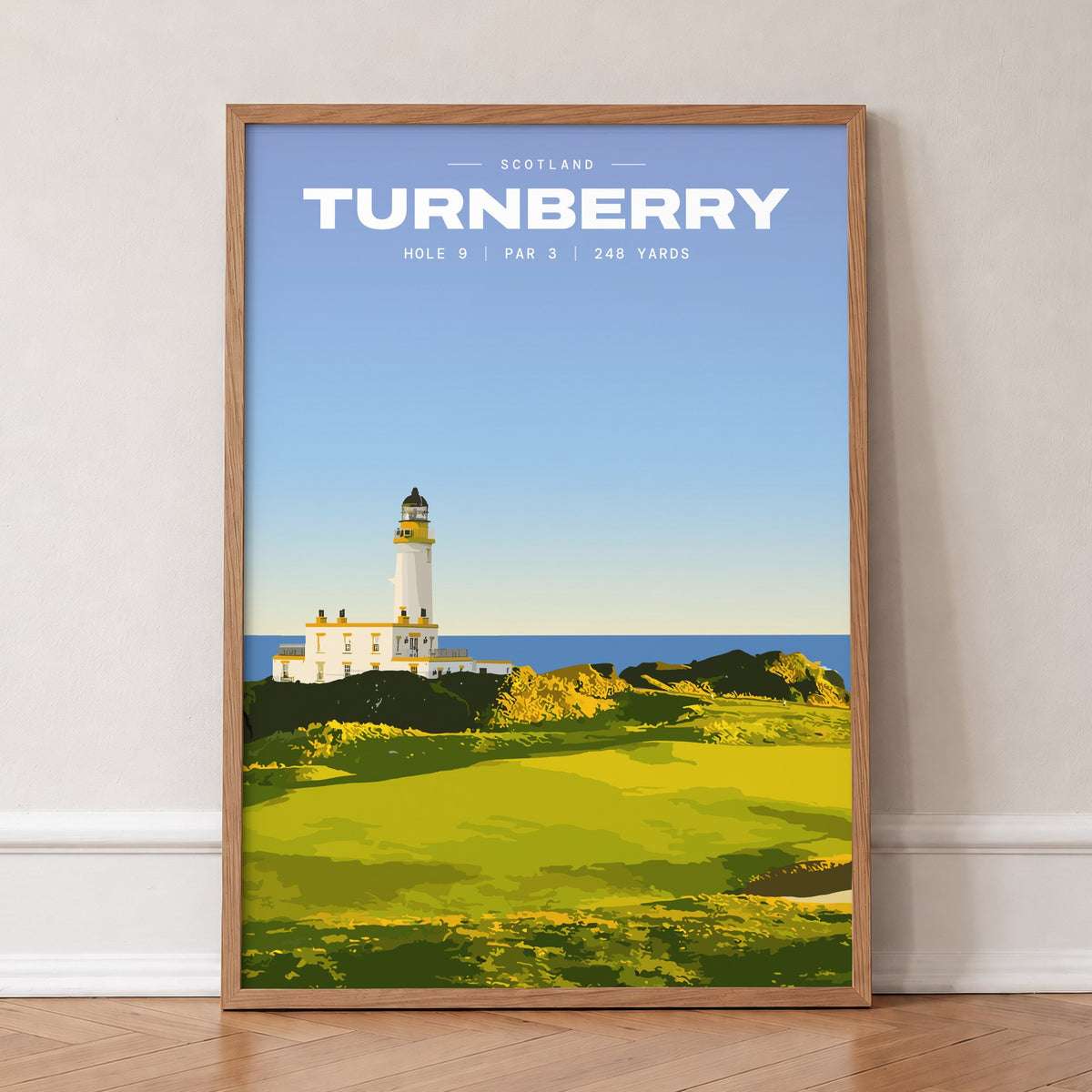 Turnberry 9th hole golf print of a white lighthouse above a links green, in an oak frame, leaning against a wall on a herringbone floor